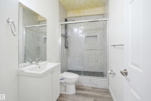Bathroom featuring a glass-enclosed shower with a recessed shelf, white vanity with integrated sink, and wood-finish flooring - 3909 49 Ave, Beaumont, AB - Indoor Photo Showing Bathroom