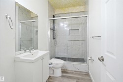 Bathroom featuring a glass-enclosed shower with a recessed shelf, white vanity with integrated sink, and wood-finish flooring - 