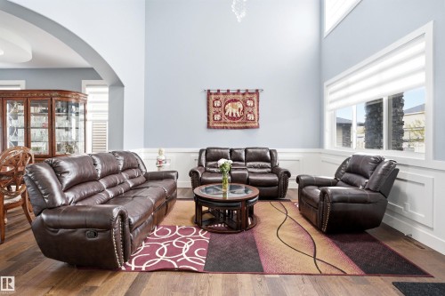 Living area featuring hardwood-style flooring, a vaulted ceiling, an arched doorway, extensive white wainscoting, and large windows with horizontal blinds - 3909 49 Ave, Beaumont, AB - Indoor Photo Showing Living Room