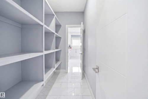 Walk in pantry with extensive built-in shelving, white paneled door with horizontal detailing, and large format tile flooring - 3909 49 Ave, Beaumont, AB - Indoor