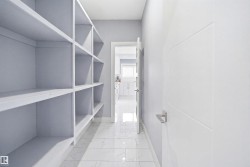 Walk in pantry with extensive built-in shelving, white paneled door with horizontal detailing, and large format tile flooring - 