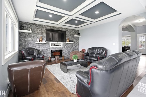 2nd Living area on the main level featuring a stone accent wall with a built-in media center, recessed lighting, coffered ceiling detail, and wood-finish flooring - 3909 49 Ave, Beaumont, AB - Indoor Photo Showing Living Room With Fireplace