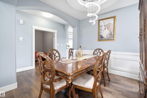 Dining area featuring wood-finish flooring, a tray ceiling with a chandelier, wainscoting, and arched doorways - 3909 49 Ave, Beaumont, AB - Indoor Photo Showing Dining Room