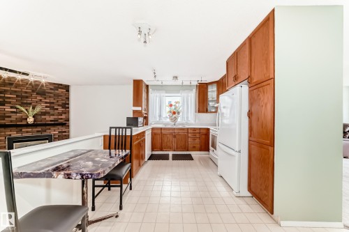 Kitchen space featuring wood cabinetry, white appliances, and light-toned square tile flooring - 14123 96 Street, Edmonton, AB 