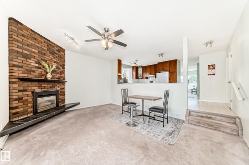 Living area featuring a brick-faced fireplace with a black tile hearth, a ceiling fan with integrated lighting, and neutral carpeting - 14123 96 Street, Edmonton, AB 