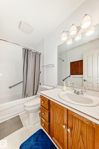Bathroom featuring a white bathtub, toilet, and a wood-finish vanity with an integrated sink and white countertop - 14123 96 Street, Edmonton, AB 