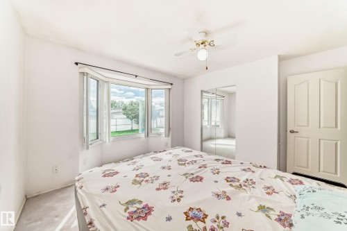 Bright interior space featuring a bay window with natural light, a ceiling fan, mirrored closet doors, a paneled interior door, and light-toned carpeting - 14123 96 Street, Edmonton, AB 
