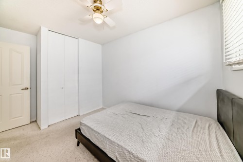 Bedroom featuring neutral carpeting, white bi-fold closet doors, a white paneled door with bronze hardware, a window with horizontal blinds, and a ceiling fan with light fixture - 14123 96 Street, Edmonton, AB 