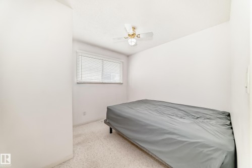Neutral-toned room featuring a single window with horizontal blinds, a ceiling fan with integrated lighting, and light-colored carpeting - 14123 96 Street, Edmonton, AB 