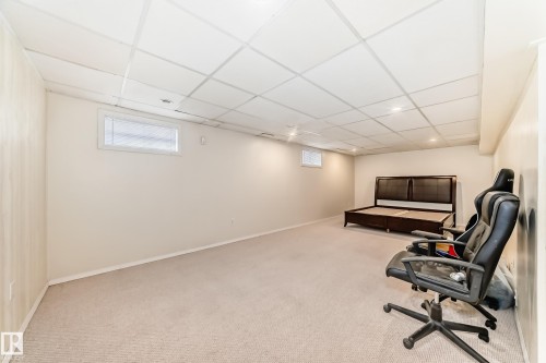 Spacious finished room featuring neutral carpeting, light-toned painted walls, and a grid panel ceiling with recessed lighting - 14123 96 Street, Edmonton, AB 