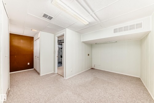 Spacious room featuring carpeting, drop ceiling with fluorescent lighting, and a built-in closet with bi-fold doors - 14123 96 Street, Edmonton, AB 