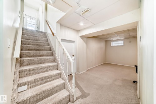 Carpeted staircase with white balusters leading to an upper level with a door featuring a glass panel - 14123 96 Street, Edmonton, AB 
