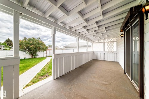 Covered patio featuring a concrete floor, slatted wood railing, decorative lattice accents, and exterior wall sconces - 14123 96 Street, Edmonton, AB 