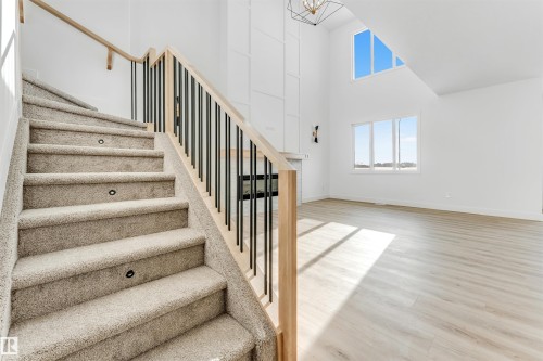 Inviting interior featuring a carpeted staircase with individual step lighting, a light wood railing, and black balusters - 4102 67 Street, Beaumont, AB - Indoor Photo Showing Other Room