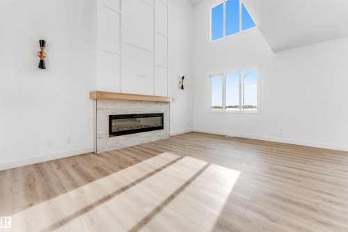 Living room featuring light-toned flooring, a fireplace with a light wood mantel and stone surround, and large windows providing natural light - 4102 67 Street, Beaumont, AB - Indoor Photo Showing Living Room With Fireplace