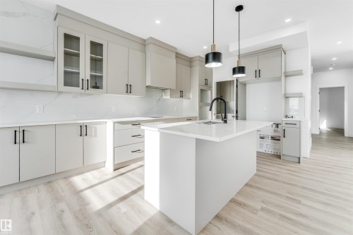 The kitchen features light-colored cabinetry with dark hardware, a large central island with a sink and a dark faucet, and light wood-style flooring - 4102 67 Street, Beaumont, AB - Indoor Photo Showing Kitchen With Upgraded Kitchen