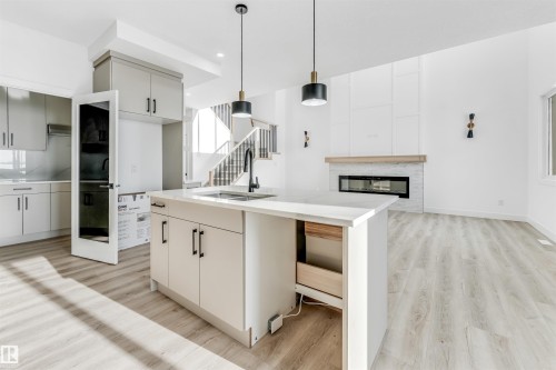 Open concept living area featuring light-colored flooring, a kitchen island with a sink and storage, and pendant lighting - 4102 67 Street, Beaumont, AB - Indoor Photo Showing Kitchen With Upgraded Kitchen