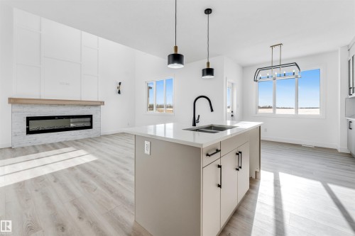 This open concept living space features light wood-style flooring and a contemporary fireplace with a wood mantel - 4102 67 Street, Beaumont, AB - Indoor With Fireplace