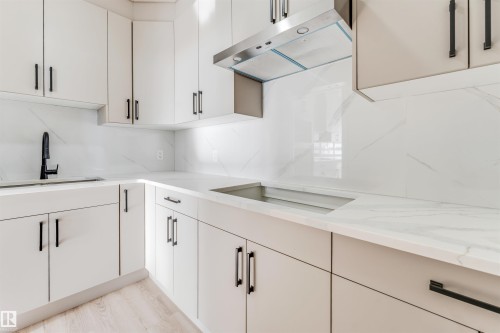 Modern kitchen featuring white cabinetry with black hardware, white countertops, a stainless steel range hood, and a black faucet - 4102 67 Street, Beaumont, AB - Indoor Photo Showing Kitchen