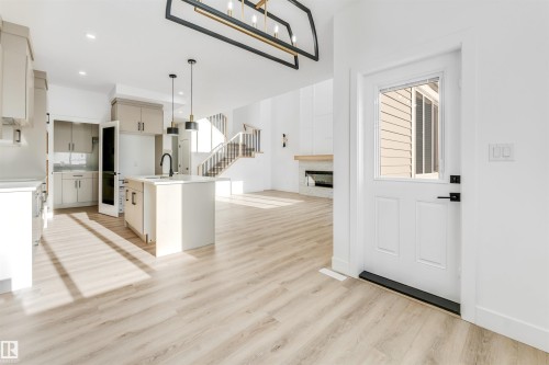 The property features an open concept layout with light wood-style flooring, a modern kitchen island with a dark faucet, and a contemporary light fixture - 4102 67 Street, Beaumont, AB - Indoor Photo Showing Kitchen