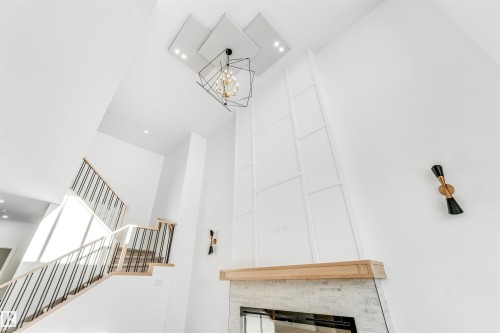 A grand interior featuring a modern chandelier, sleek wall sconces, and a contemporary fireplace with a light wood mantel - 4102 67 Street, Beaumont, AB - Indoor Photo Showing Other Room With Fireplace
