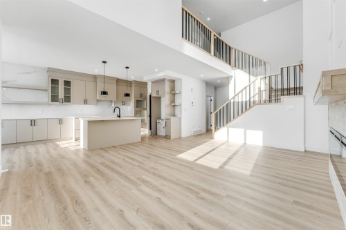 The property features an open-concept layout with light-toned flooring, a kitchen island with a sink, and a staircase with light wood and black railings - 4102 67 Street, Beaumont, AB - Indoor Photo Showing Kitchen With Upgraded Kitchen