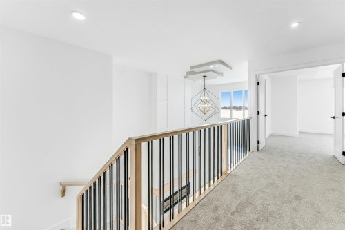The property features a staircase with a natural wood handrail and black vertical balusters, leading to a carpeted landing - 4102 67 Street, Beaumont, AB - Indoor Photo Showing Other Room