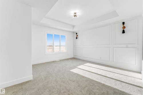 Spacious room featuring a tray ceiling, wall sconces, detailed wall molding, and a large window providing ample natural light - 4102 67 Street, Beaumont, AB - Indoor Photo Showing Other Room