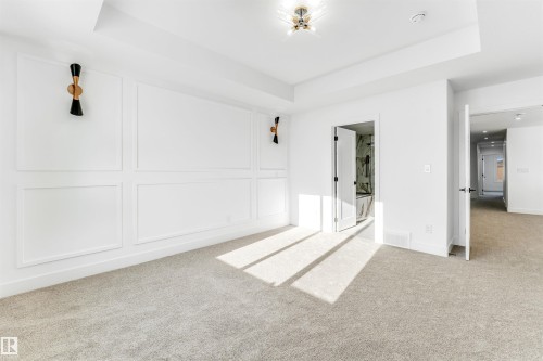 Spacious room featuring white walls with decorative paneling, light-colored carpet, a modern ceiling light fixture, and wall-mounted sconces - 4102 67 Street, Beaumont, AB - Indoor Photo Showing Other Room