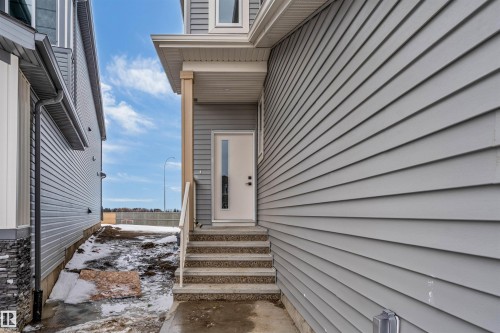 The property features gray horizontal siding and a front entry door with a rectangular window insert - 4102 67 Street, Beaumont, AB - Outdoor With Exterior