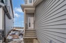 The property features gray horizontal siding and a front entry door with a rectangular window insert - 4102 67 Street, Beaumont, AB  - Outdoor With Exterior 