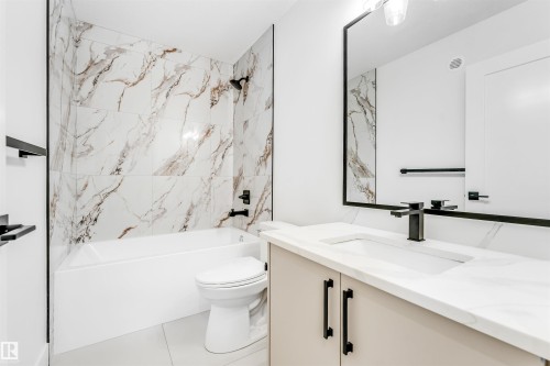 Bathroom featuring a bathtub with a tiled surround, a toilet, a vanity with a rectangular sink, and a framed mirror - 4102 67 Street, Beaumont, AB - Indoor Photo Showing Bathroom