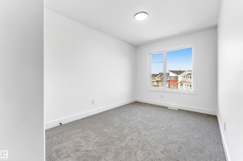 This room features neutral-toned carpet flooring, white walls, and a large window providing views of nearby properties - 4102 67 Street, Beaumont, AB - Indoor Photo Showing Other Room