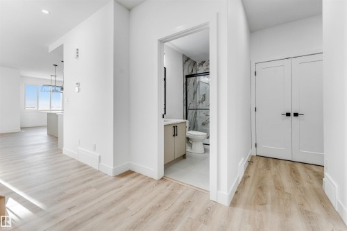The property features light-toned flooring throughout, with a bathroom showcasing a vanity, toilet, and a shower with a dark-framed enclosure and patterned wall tiles - 4102 67 Street, Beaumont, AB - Indoor Photo Showing Other Room