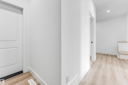 The property features light wood flooring throughout the hallway, white painted walls and trim, and a white interior door - 4102 67 Street, Beaumont, AB - Indoor Photo Showing Other Room