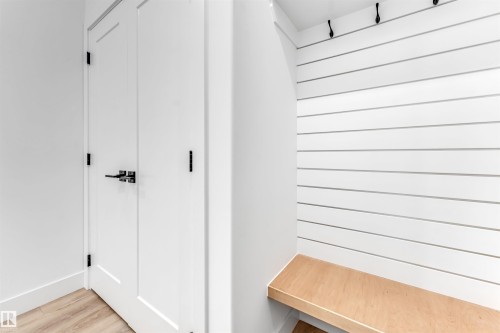 Entryway featuring light hardwood flooring, white painted doors with black hardware, and a built-in bench with white shiplap paneling and black coat hooks - 4102 67 Street, Beaumont, AB - Indoor Photo Showing Other Room