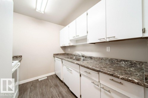 Kitchen featuring white cabinetry with brushed nickel hardware, dual basin stainless steel sink, dark patterned countertops, and wood-finish flooring - 17106 108 St Nw, Edmonton, AB - Indoor Photo Showing Kitchen With Double Sink