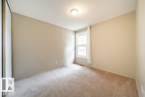 Carpeted room featuring a double-paned window, neutral wall tones, a ceiling-mounted light fixture, and a built-in closet with sliding doors - 17106 108 St Nw, Edmonton, AB - Indoor Photo Showing Other Room