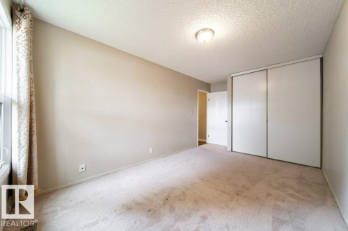 Carpeted room featuring a window with patterned curtains, neutral wall paint, a built-in closet with sliding doors, and a ceiling-mounted light fixture - 17106 108 St Nw, Edmonton, AB - Indoor Photo Showing Other Room