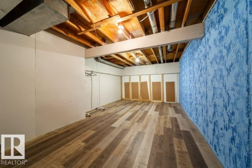 Spacious interior featuring wood-finish flooring, exposed ceiling joists, and a decorative textured accent wall - 17106 108 St Nw, Edmonton, AB - Indoor