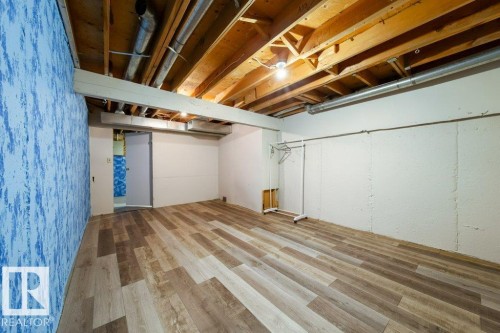 Spacious room featuring wood-finish flooring, exposed ceiling joists, and a partial blue textured accent wall - 17106 108 St Nw, Edmonton, AB - Indoor Photo Showing Basement