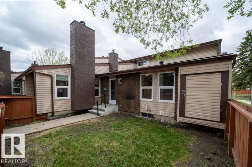 Rear exterior featuring light beige siding, exposed brick accents, and a prominent brown chimney structure - 17106 108 St Nw, Edmonton, AB - Outdoor