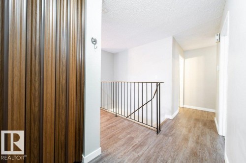 Upper-level hallway featuring wood-finish flooring, white baseboards, and a black wrought iron railing - 17106 108 St Nw, Edmonton, AB - Indoor Photo Showing Other Room