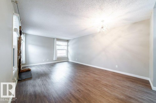 Spacious room featuring wood-finish flooring, a contemporary chandelier, multiple windows with white blinds, and a built-in fireplace structure - 17106 108 St Nw, Edmonton, AB - Indoor Photo Showing Other Room