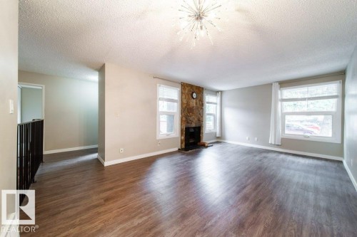 Spacious living area featuring wood-finish flooring, a stone-clad fireplace, and multiple windows - 17106 108 St Nw, Edmonton, AB - Indoor Photo Showing Living Room With Fireplace