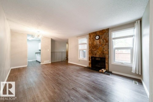 Living area featuring wood-finish flooring and a stone-clad fireplace with a dark hearth - 17106 108 St Nw, Edmonton, AB - Indoor Photo Showing Living Room With Fireplace