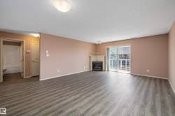 Spacious living area featuring wood-finish flooring, a corner fireplace with a white mantel, and sliding glass doors opening to the exterior - 
