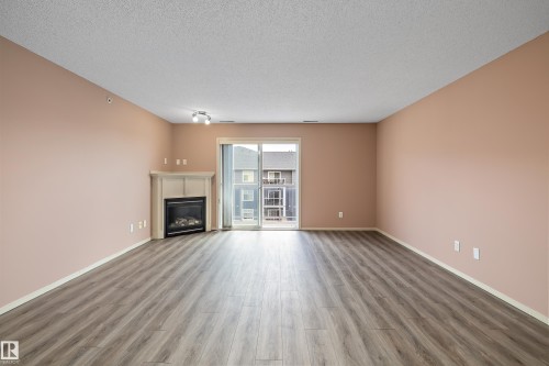Spacious room featuring wood-finish flooring, a corner fireplace with a mantel, and a sliding glass door - 406 16035 132 Street, Edmonton, AB - Indoor Photo Showing Living Room With Fireplace