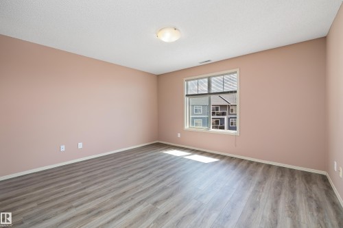 Spacious room featuring wood-finish flooring, a large window with blinds, and a flush-mount ceiling light fixture - 406 16035 132 Street, Edmonton, AB - Indoor Photo Showing Other Room