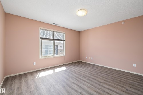 Spacious room featuring wood-finish flooring, a large window with blinds, and neutral-colored walls - 406 16035 132 Street, Edmonton, AB - Indoor Photo Showing Other Room
